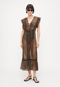 Vestido de tela transparente con estampado de leopardo, mangas con volantes, cintura con lazo y dobladillo escalonado. Combinado con gafas de sol negras y sandalias planas.