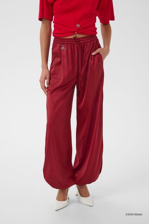 Osoba ubrana w luźne, błyszczące ciemnoczerwone spodnie ze ściągaczami na końcach, dopasowany krótki czerwony top oraz białe wysokie obcasy z szpiczastym noskiem.