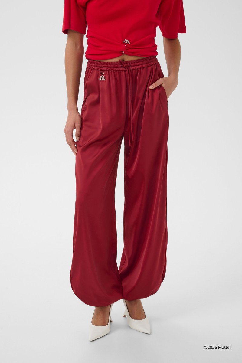 Άτομο που φοράει άνετο, γυαλιστερό σκούρο κόκκινο παντελόνι με ελαστικά τελειώματα, ταιριαστό κοντό κόκκινο τοπ και λευκά μυτερά ψηλοτάκουνα παπούτσια.