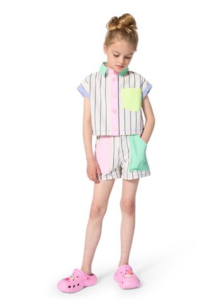 Bijgesneden overhemd met knopen in pasteltinten en fijne strepen, gecombineerd met bijpassende shorts; beide hebben zakken van contrasterende stof. Roze klompen.