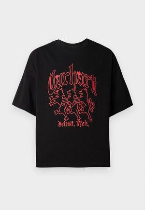 Must musta särk lühikeste varrukatega, mis on valmistatud puuvillast, koos julge punase graafikaga, kus on kujutatud kolme lõvi ja tekst "Carhartt, Detroit, Mich."