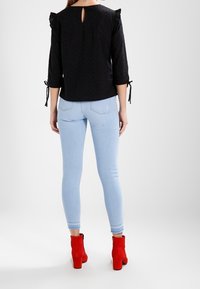 Černá blůza s volánkovými rukávy a výstřihem na zádech, doplněná světle modrými úzkými džíny a červenými vysokými kotníkovými botami.