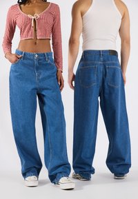 Wide-leg blue denim jeans with a loose fit, featuring side pockets and rear pockets, paired with white sneakers.