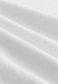 Gros plan sur un tissu blanc avec une fine texture côtelée en diagonale et des plis doux.