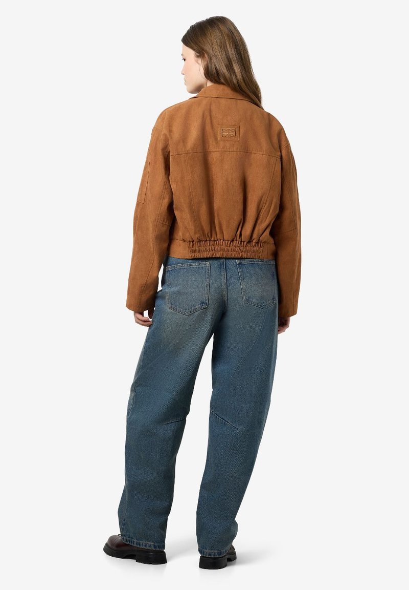 Veste en daim marron courte avec une taille élastique, associée à un jean évasé bleu clair avec un motif texturé et des poches.