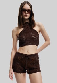 Top halter tejido a ganchillo en color marrón con detalle floral en el escote, combinado con pantalones cortos a juego con patrones de diamante y cintura con cordón.