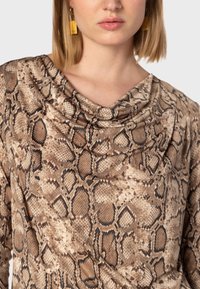 Top marrone a stampa serpente con scollo a cappuccio, caratterizzato da un tessuto testurizzato e un design drappeggiato. Accentuato da orecchini abbinati.