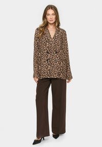 Blazer s leopardím vzorom s dvojradovým zapínaním, ktorý má čierne gombíky, dlhé rukávy a voľný strih, kombinovaný s hnedými nohavicami s širokými nohavicami.
