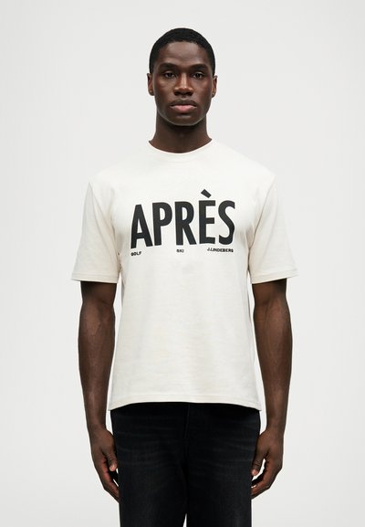T-shirt crema a maniche corte con il bold del testo nero "APRÈS GOLF SKI J.LINDBERG" sul davanti. Collo a giro e vestibilità rilassata.