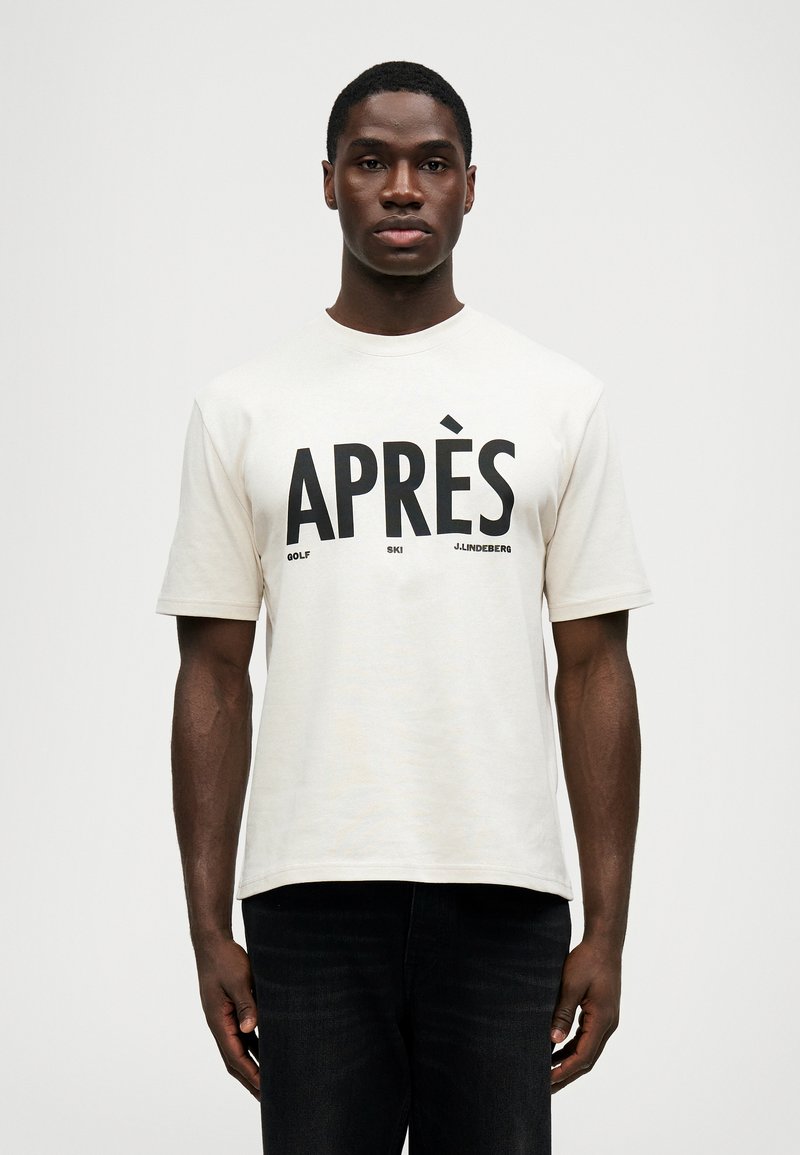 T-shirt de manga curta creme com texto em preto em destaque "APRÈS GOLF SKI J.LINDBERG" na parte frontal. Gola redonda e corte descontraído.