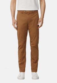 Chino in cotone marrone con vestibilità slim, dotati di chiusura a bottone, passanti per cintura e tasche laterali. Abbinati a sneakers bianche.