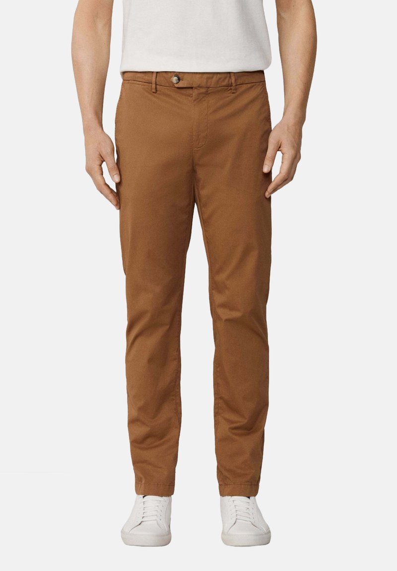 Chino in cotone marrone con vestibilità slim, dotati di chiusura a bottone, passanti per cintura e tasche laterali. Abbinati a sneakers bianche.