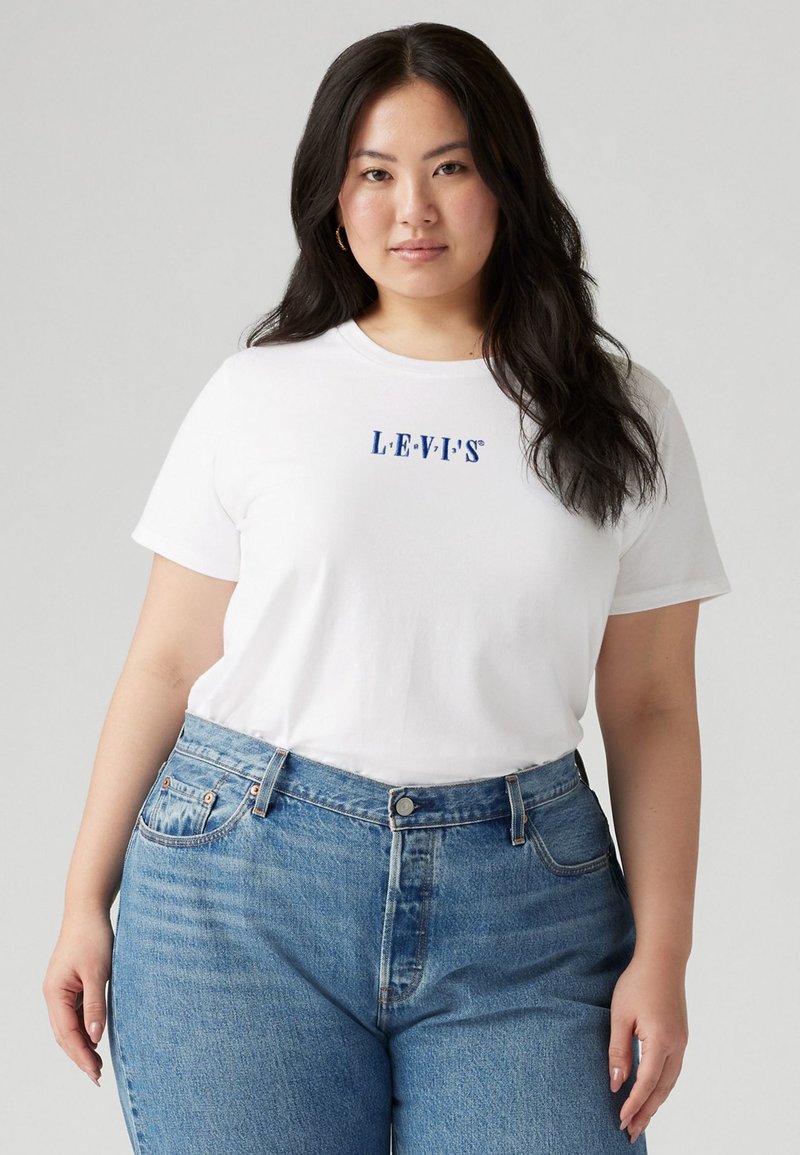 White cotton t-shirt with blue "LEVI'S" logo, paired with medium-wash high-waisted denim jeans. Model stands against a neutral background.