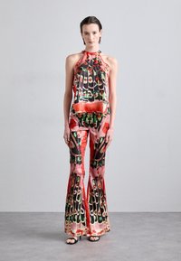 Top à col halter et pantalon évasé en tissu léger et coloré avec des motifs floraux et abstraits en rouge, vert et noir.