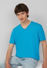 T-shirt V-neck azzurro cielo, maniche corte, texture liscia, logo sul petto sinistro, abbinato a pantaloni corti in denim blu chiaro.