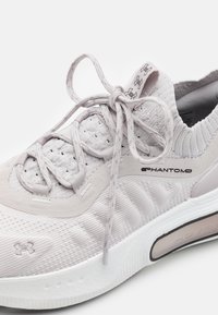 Chaussure de course Under Armour Phantom gris clair avec tige en mesh, fermeture à lacets et semelle blanche amortie.