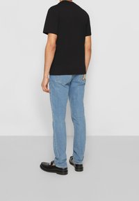 Svart bomulls-T-shirt med kort ärm, kombinerad med ljusblå rak benjeans som har en tecknad grafik på bakfickan.