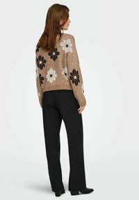 Suéter beige de punto con grandes patrones florales en blanco y negro; se lleva con pantalones negros; presenta un corte relajado y puños de canalé.