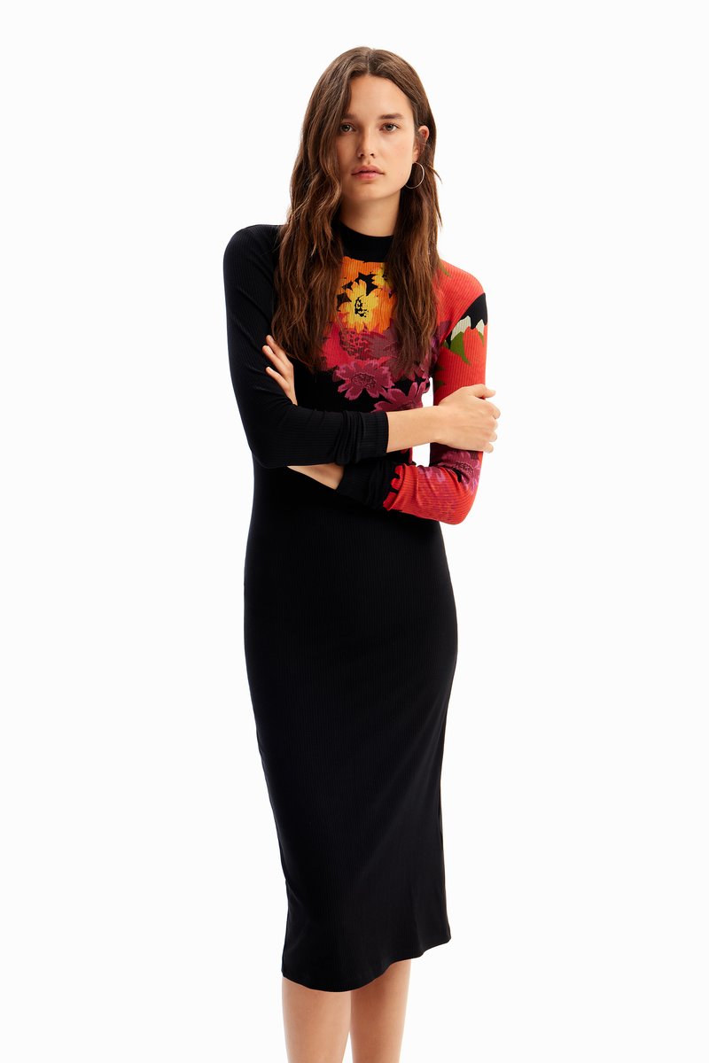 Czarna sukienka midi z prążkowanej tkaniny, z długimi rękawami; jeden z rękawów zdobi kolorowy wzór w kwiaty. Dopasowany krój, okrągły dekolt.