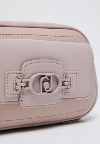 Borsa a mano in pelle rosa chiaro con finitura testurizzata, dotata di una chiusura prominente con design circolare e cuciture intricate lungo i bordi.