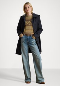 Trench coat azul marino, suéter de punto estampado en tonos tierra, jeans sueltos de color azul claro, cinturón marrón y botas marrones. Texturas suaves y corte estructurado.