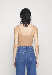 Braunes Crop-Top mit dünnen Trägern und geriffeltem Rücken, kombiniert mit hochgeschnittenen blauen Jeans aus Denim, die mit Gesäßtaschen und einem leicht lockeren Schnitt ausgestattet sind.