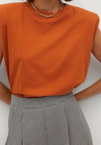 Haut orange sans manches avec un col rond, associé à une jupe à carreaux noir et blanc taille haute.