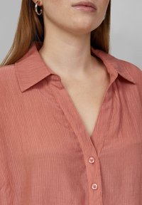Stoffen shirt in stoffige roze kleur met een kraag, voorzien van een knoopsluiting en subtiele verticale strepen.