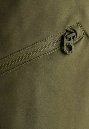 Tela verde con un bolsillo con cremallera que tiene un tirador redondo etiquetado "Joules". La textura es suave, con una costura resistente.