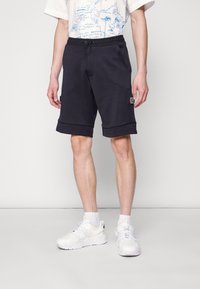 Granatowe szorty z mieszanki bawełny z elastycznym pasem, z bocznymi kieszeniami i ozdobną naszywką na lewej udzie.