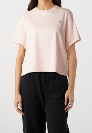 Kvinde iført en lyserød kortærmet cropped t-shirt med et lille trekantet logo på brystet og højtaljede sorte jeans.