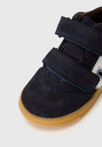Granatowe zamszowe buty dziecięce z dwoma rzepami, jasnobrązową gumową podeszwą i niebieskimi detalami szwów wzdłuż krawędzi.