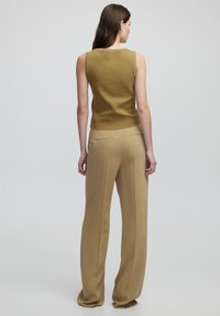 Top sin mangas de color verde oliva con un acabado texturizado, combinado con pantalones fluidos de color beige claro que cuentan con bolsillos traseros y un corte recto.