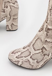 Beige enkellaarsjes met een gestructureerd slangprintpatroon, voorzien van een chunky hak en een spitse neus, met een rits aan de zijkant.