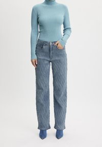 Jasnoniebieski prążkowany sweter z golfem i długimi rękawami, w połączeniu z fakturowanymi, ciemnoniebieskimi spodniami typu quilted. Modelka nosi niebieskie botki za kostkę.