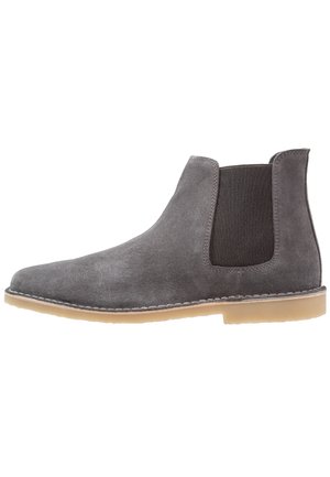 Bottes Chelsea en daim gris avec panneau latéral élastique, semelle en caoutchouc beige et détails cousus le long du bord de la semelle.