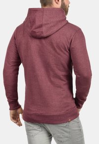 Sudadera burdeos con capucha ajustable. Textura suave, mangas largas y dobladillo acanalado. Presenta un pequeño detalle de logo cerca de la cinturilla.