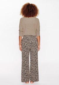 Top beige a maniche lunghe abbinato a pantaloni larghi e morbidi con un motivo a stampa leopardata nera e marrone. Tessuto morbido e vestibilità rilassata.
