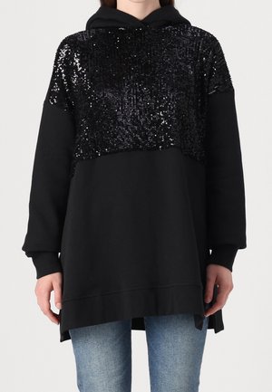 Sweat à capuche noir avec un panneau supérieur noir à sequins brillants, manches longues et fentes latérales, porté avec un jean bleu.