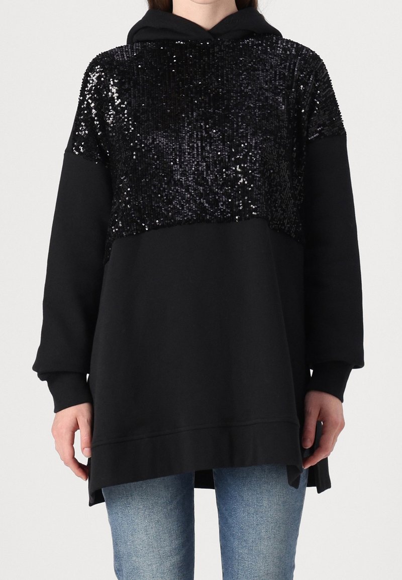 Sweat à capuche noir avec un panneau supérieur noir à sequins brillants, manches longues et fentes latérales, porté avec un jean bleu.