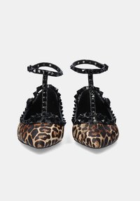 Bailarinas con estampado de leopardo y acentos de cuero negro brillante. Cuentan con una punta afilada, detalles de tachuelas a lo largo del empeine y una correa al tobillo.