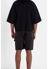 T-shirt nera oversize con maniche corte, abbinata a pantaloni cargo in denim scuro con tasche e orlo sfilacciato. Design semplice e moderno.