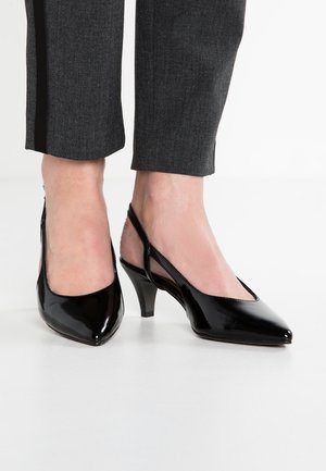 Czarne lakierowane szpilki typu slingback z szpiczastym noskiem, średnim obcasem i gładkim, błyszczącym wykończeniem. W połączeniu z grafitowymi spodniami.