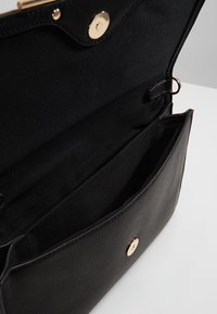 Svart läderhandväska öppen för att visa det rymliga interiören med tygfoder och guldtonad magnetisk tryckknapp.