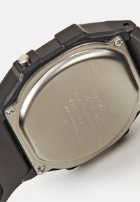 Montre-bracelet en résine noire avec un dos en acier inoxydable, présentant des détails gravés et une conception résistante à l'eau. Forme et texture minimalistes.