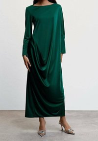 Grünes Satin-Kleid mit lockerem, gerafftem Design, langen Ärmeln und weitem Ausschnitt, kombiniert mit klaren, spitzen High Heels mit dekorativer Schnalle.