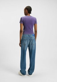 Paarse aangesloten t-shirt gecombineerd met losse blauwe spijkerbroek. De jeans hebben twee achterzakken en een blauw logo label op de tailleband.