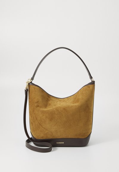 Sac en daim jaune moutarde avec une base et une sangle d'épaule en cuir marron foncé lisse. Accents en métal doré et nom de la marque embossé.