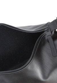 Borsa impermeabile nera con texture liscia e opaca, chiusura a zip e rivestimento in tessuto. Presenta un design elegante con un accento di logo.