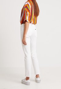 Bílé slim-fit kalhoty spárované s barevně pruhovanou blůzou s krátkým rukávem. Bílá sportovní obuv dotváří celý outfit.